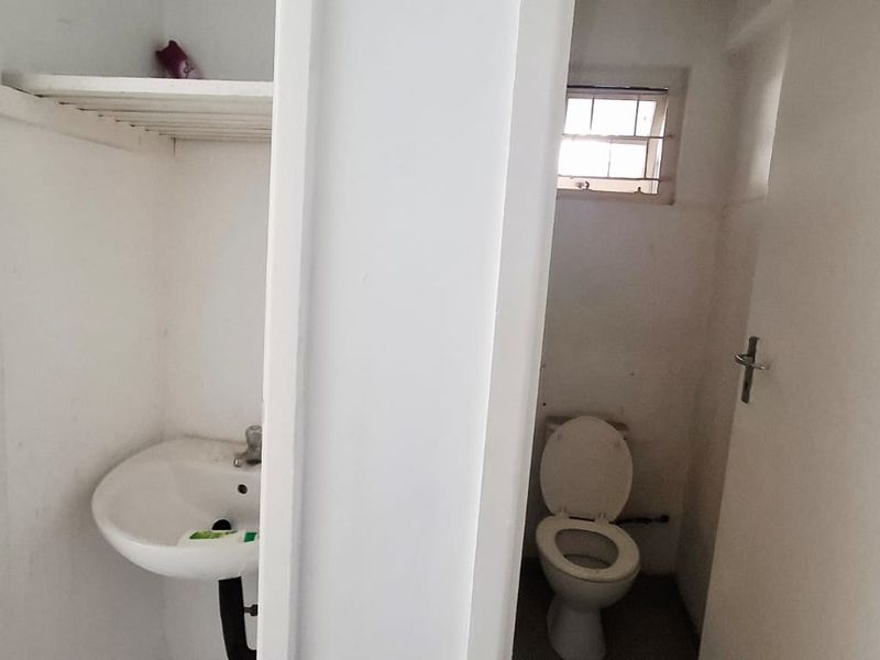 A functional bathroom featuring a pedestal washbasin, toilet, and built-in shelving, requiring cosmetic updates to improve its overall condition.