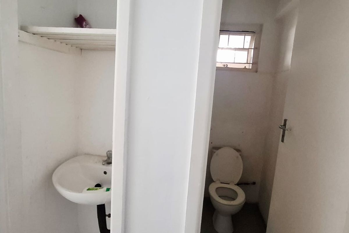 A functional bathroom featuring a pedestal washbasin, toilet, and built-in shelving, requiring cosmetic updates to improve its overall condition.