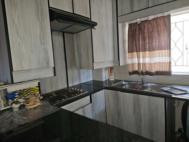 Functional kitchen featuring wood-look cabinetry, dark granite countertops, an integrated electric hob with extractor fan, and a stainless steel sink.