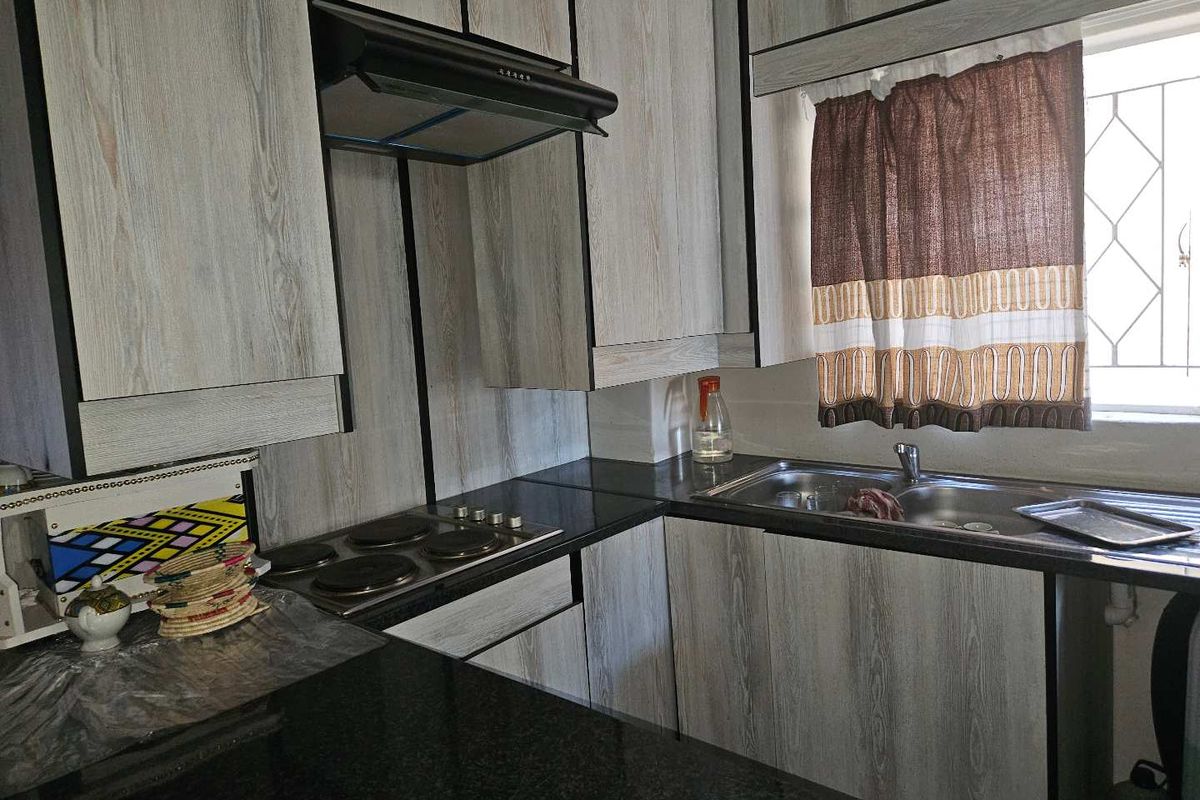 Functional kitchen featuring wood-look cabinetry, dark granite countertops, an integrated electric hob with extractor fan, and a stainless steel sink.