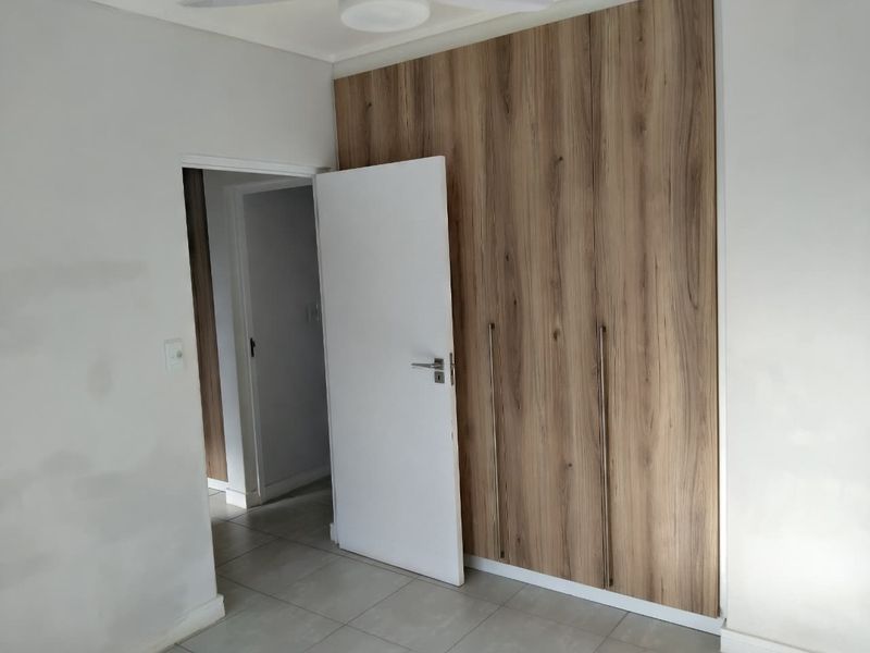 A bedroom featuring modern wood-finish built-in cupboards and tiled flooring, currently vacant and awaiting final wall finishing touches.