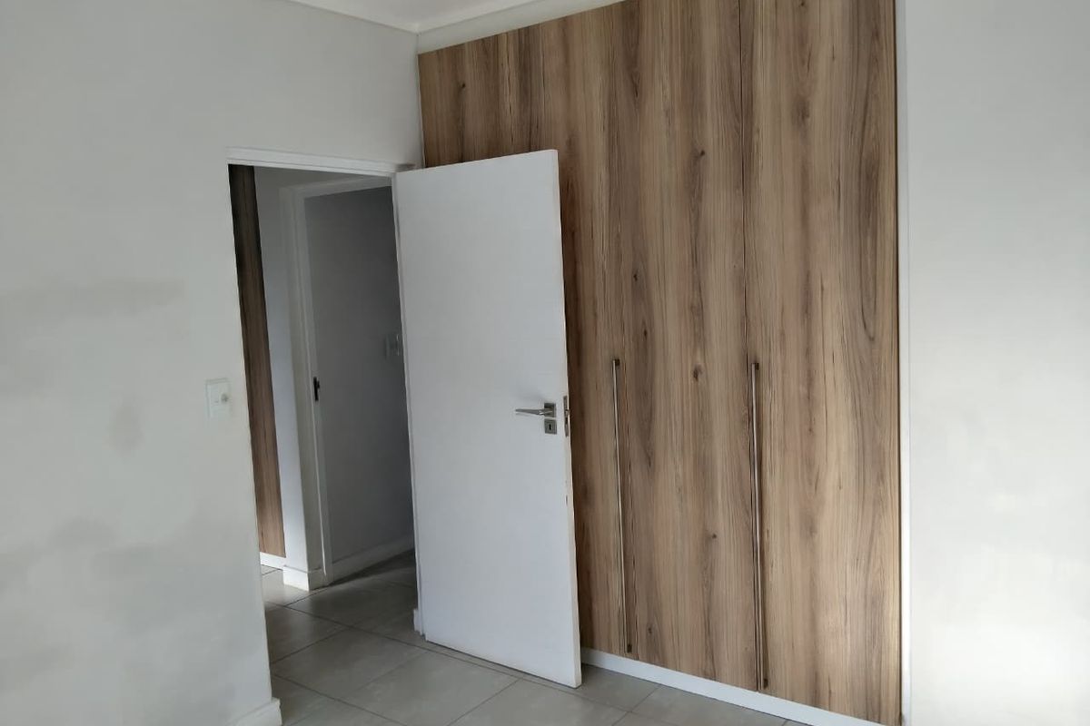 A bedroom featuring modern wood-finish built-in cupboards and tiled flooring, currently vacant and awaiting final wall finishing touches.