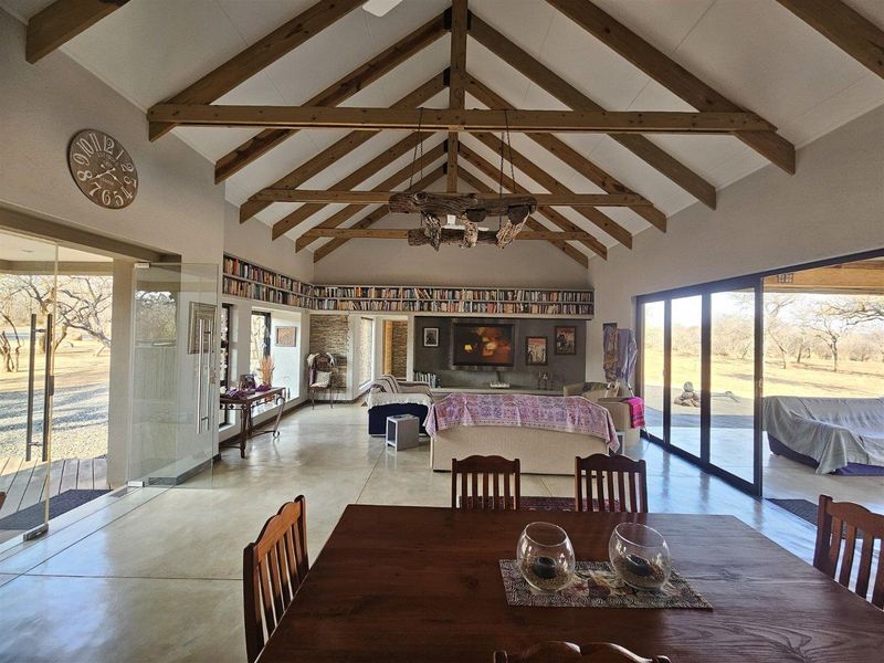 Spacious open-plan living area featuring a vaulted ceiling with exposed timber trusses, polished concrete floors, and expansive sliding glass doors leading to the outdoors.