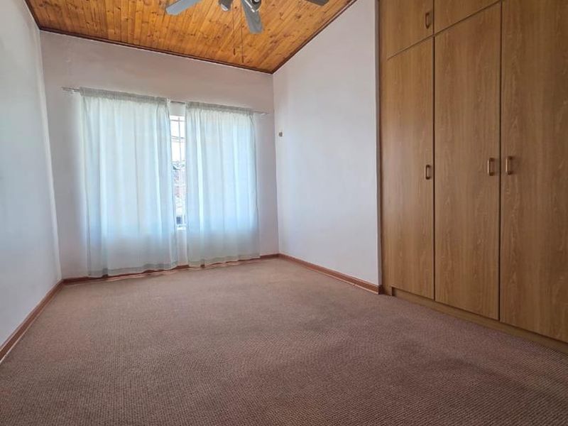 A vacant bedroom featuring a timber-clad ceiling, ceiling fan, and built-in wooden cupboards with carpeted flooring.