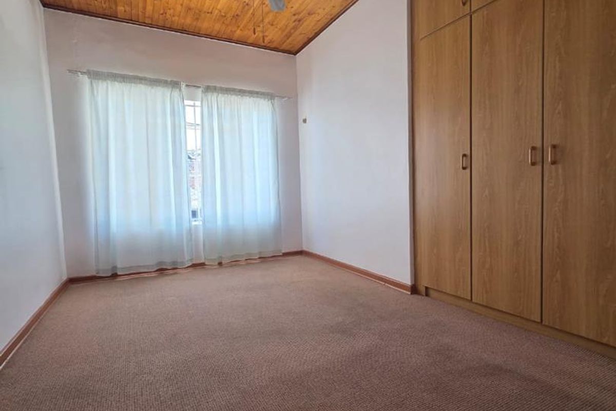A vacant bedroom featuring a timber-clad ceiling, ceiling fan, and built-in wooden cupboards with carpeted flooring.
