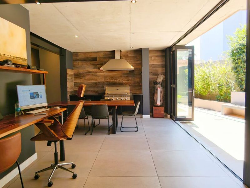 Modern open-plan living area featuring a built-in braai, sleek tiled flooring, and large stacking doors that open onto a private patio.