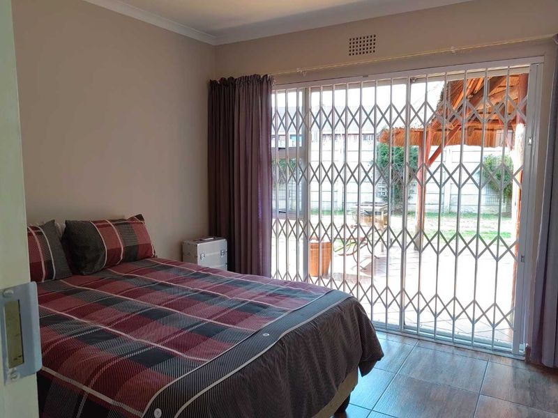 A bedroom featuring tiled flooring and a sliding glass door with a security gate, providing direct access to the outdoor patio area.