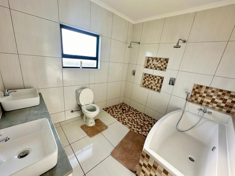 Modern bathroom featuring a double vanity with vessel sinks, a spacious walk-in shower with built-in niches, and a separate bathtub.
