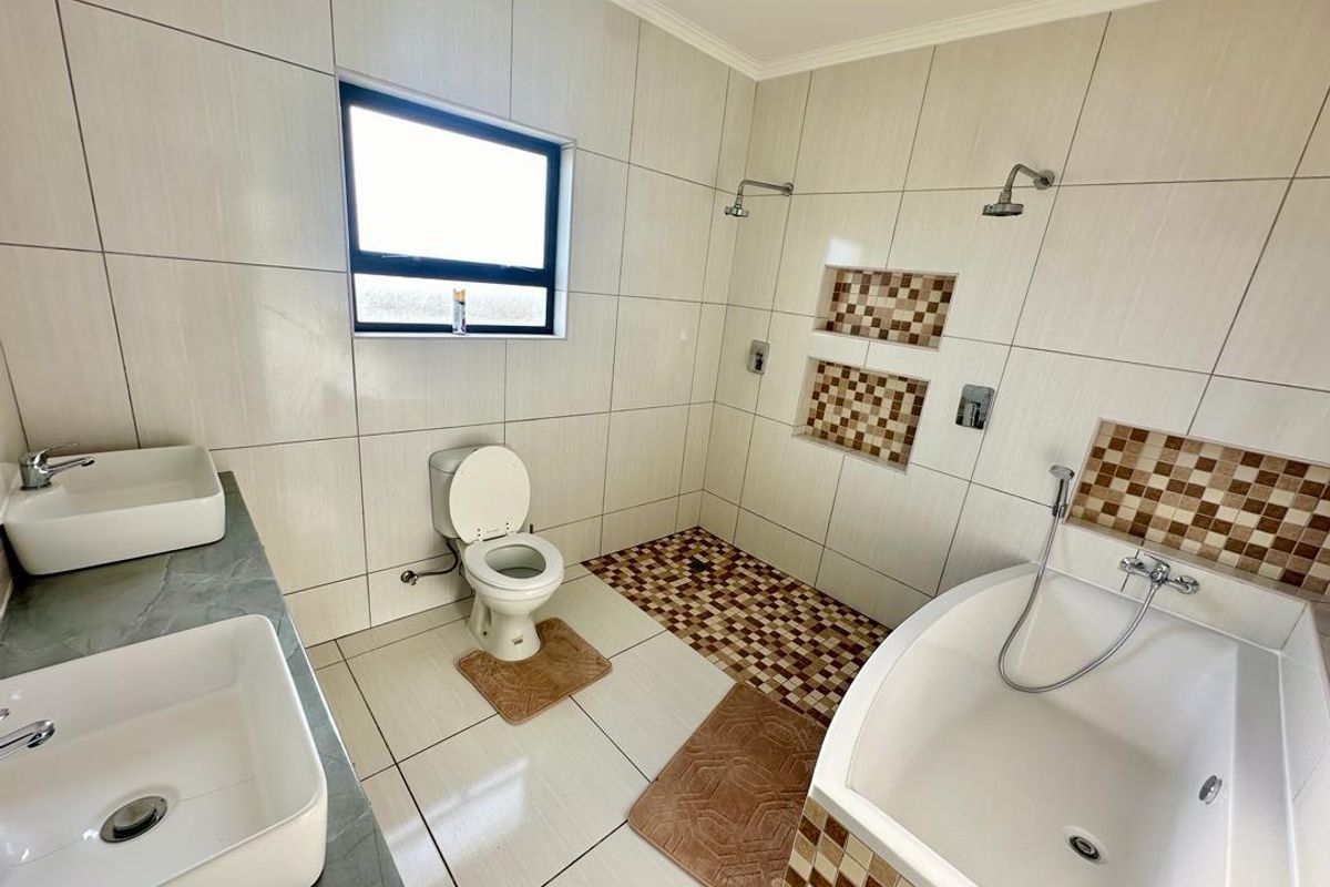 Modern bathroom featuring a double vanity with vessel sinks, a spacious walk-in shower with built-in niches, and a separate bathtub.