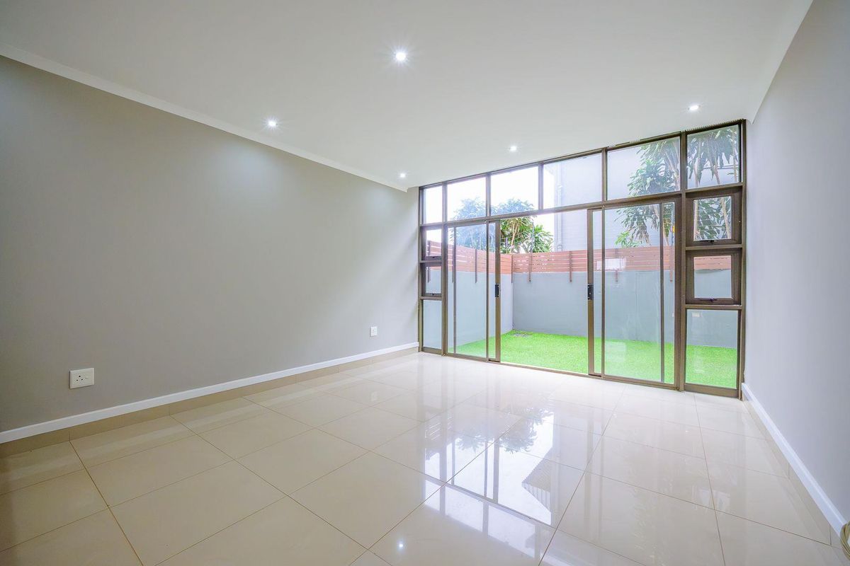 A bright, empty living room featuring polished tiled flooring, recessed lighting, and large aluminium sliding doors providing direct access to a private garden area.