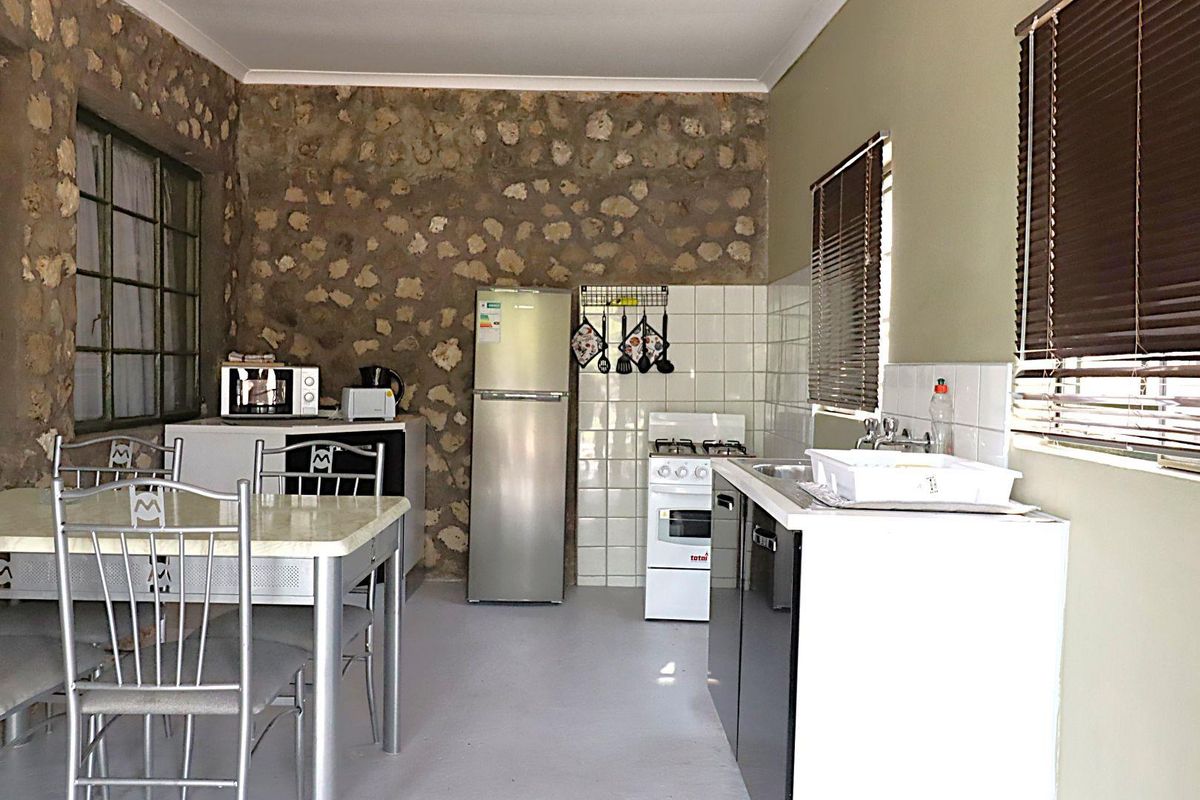 A functional kitchen area featuring a rustic stone feature wall, tiled splashbacks, and built-in cabinetry with a freestanding stove.