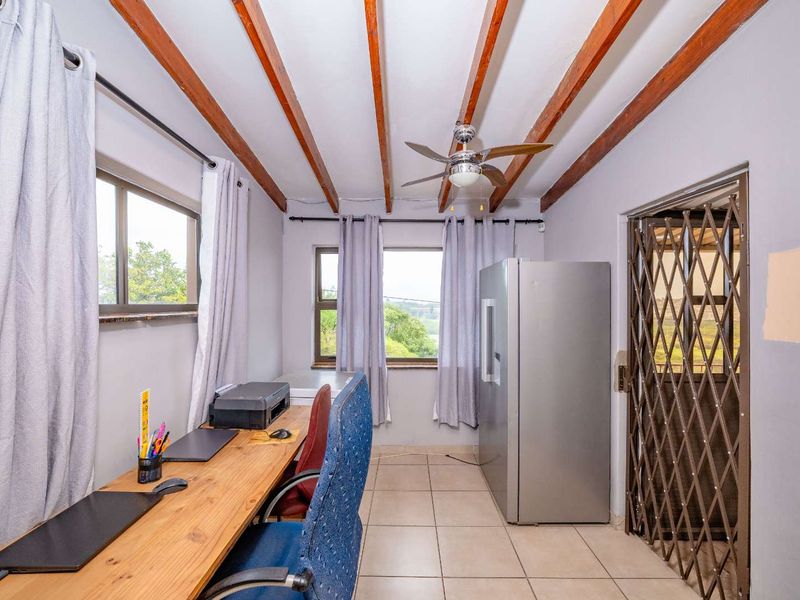 A functional office space featuring exposed timber ceiling beams, tiled flooring, and a ceiling fan, with access through a secure metal gate.