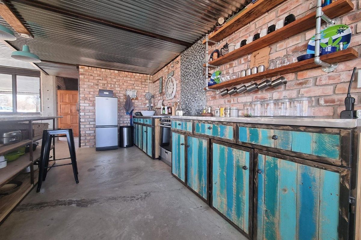 Industrial-style kitchen featuring exposed brick walls, corrugated metal ceiling, custom distressed timber cabinetry, and open shelving with integrated stainless steel countertops.