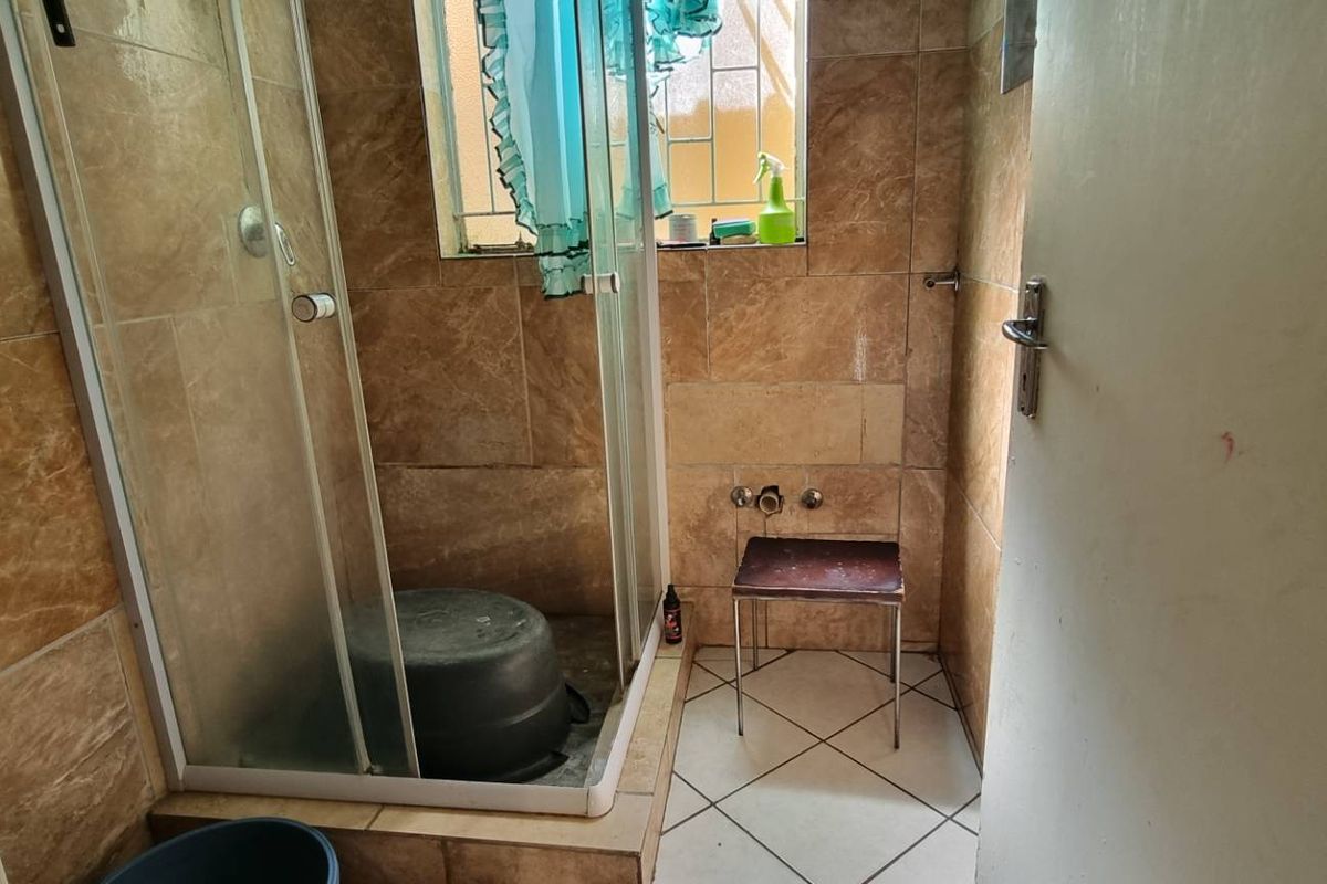 A compact bathroom featuring a glass shower enclosure, full-height wall tiling, and tiled flooring with a window for natural light.