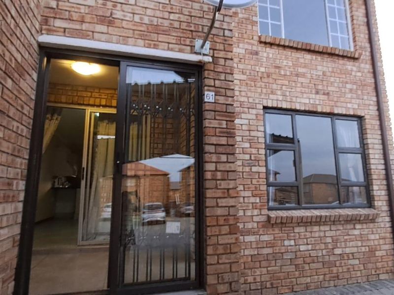 Front elevation of a face brick townhouse featuring a sliding glass entrance door, security gate, and aluminium-framed windows.