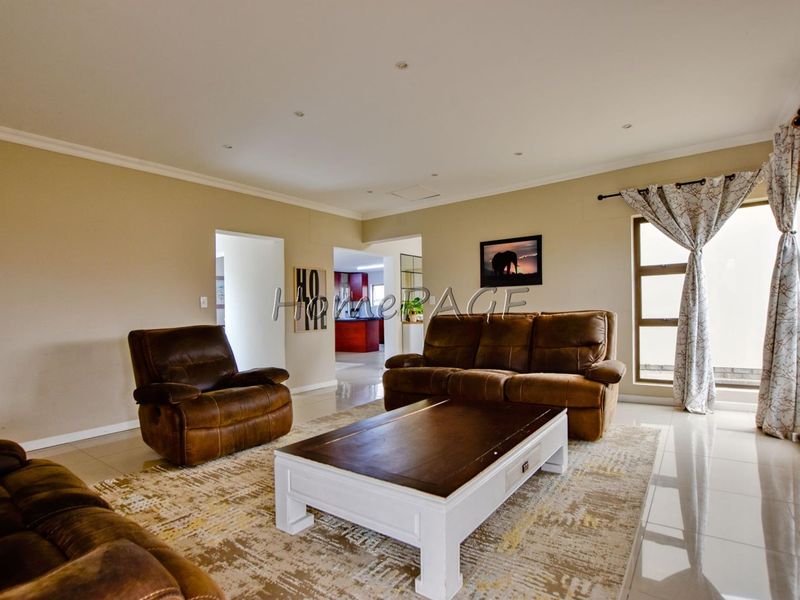 Spacious living room featuring neutral walls, tiled flooring, and recessed downlights, with a view through to the kitchen area.