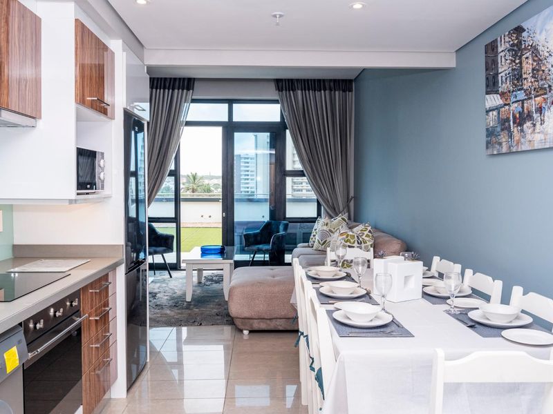 Modern open-plan apartment featuring a sleek kitchen with built-in appliances, flowing into a dining area and living space with access to a private balcony.