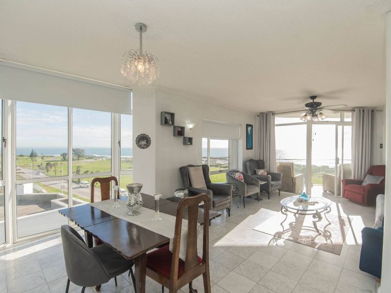 Spacious open-plan living and dining area featuring large windows with panoramic coastal views, tiled flooring, and direct access to a balcony.
