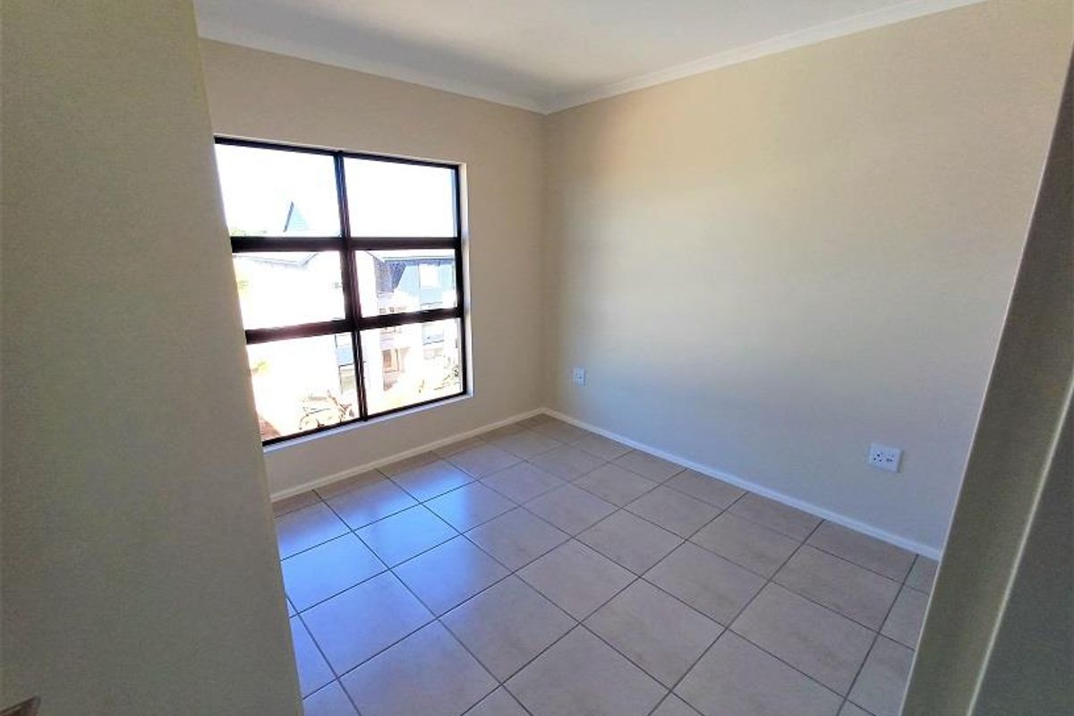 A bright, empty bedroom featuring neutral wall paint, tiled flooring, and a large window providing natural light.