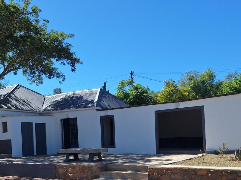 A well-maintained rear exterior view of the guest house featuring a paved patio area, stone retaining walls, and a classic corrugated metal roof.