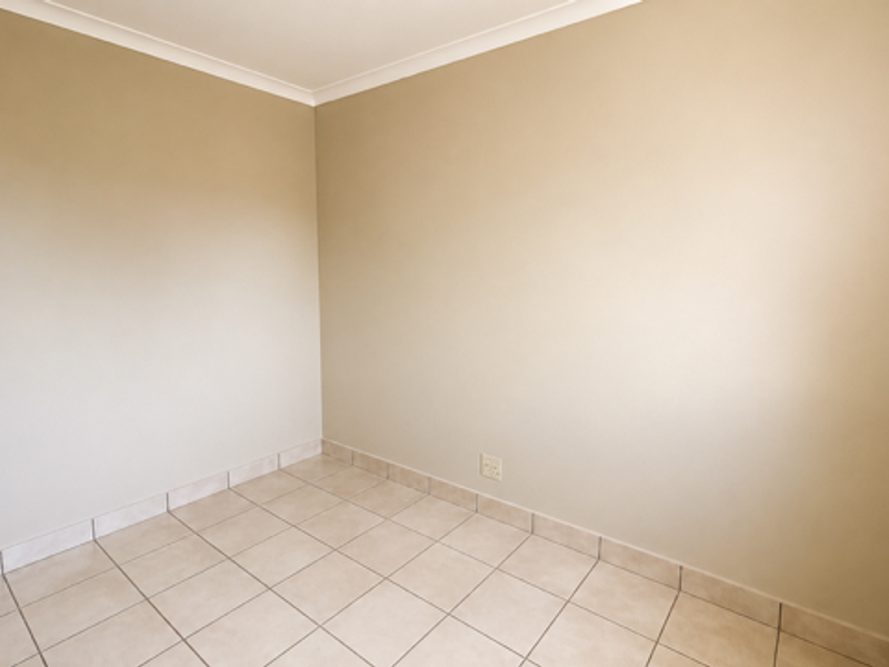 A clean, empty bedroom featuring neutral wall paint, tiled flooring, and coved ceiling detailing, providing a versatile blank canvas for personalization.