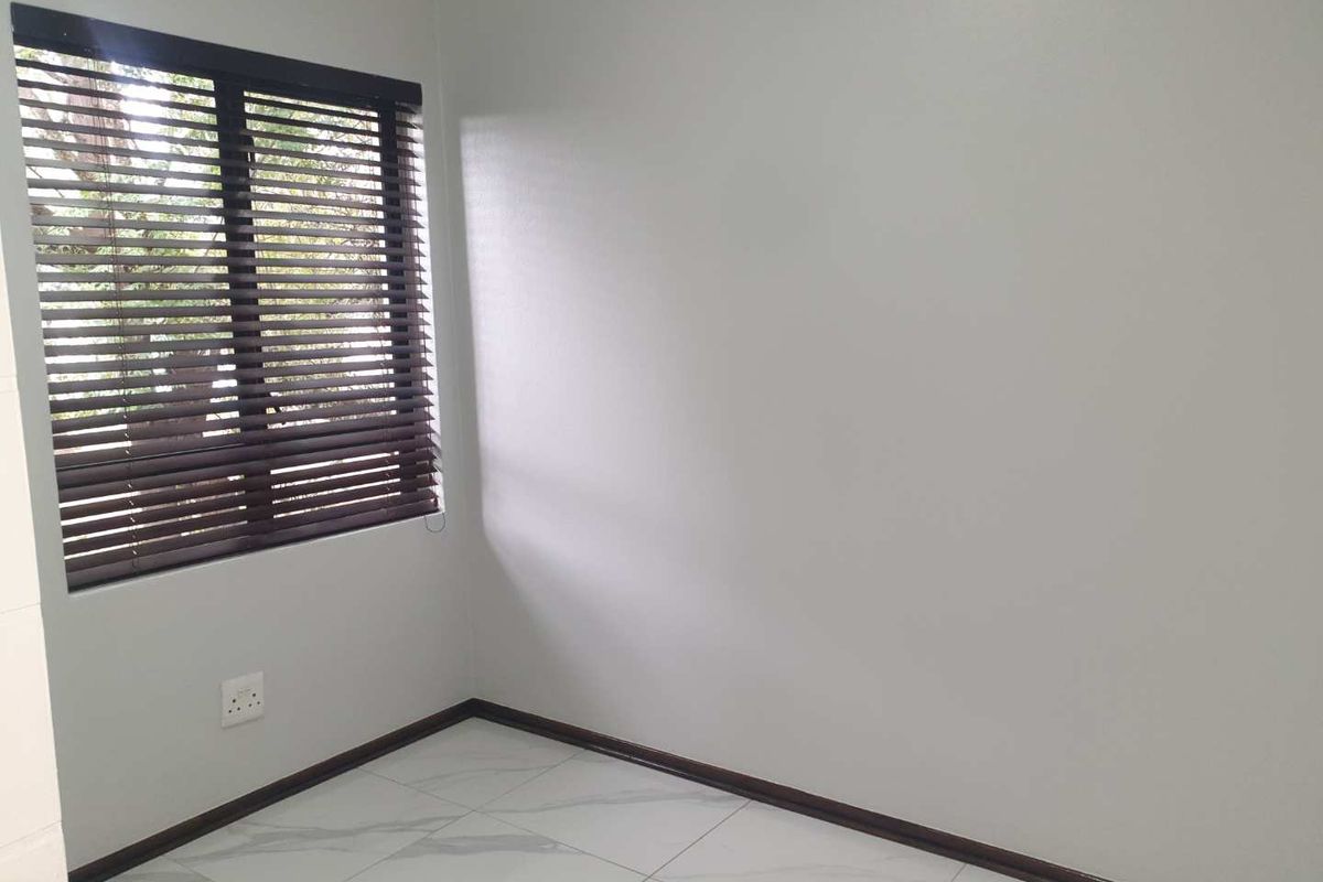 A bright, empty bedroom featuring modern white marble-look floor tiles, neutral walls, and dark wooden venetian blinds.