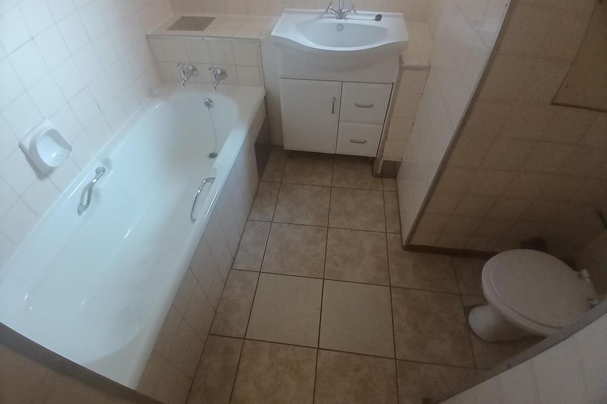 A functional bathroom featuring a bathtub, vanity basin, and toilet with tiled finishes, presenting an opportunity for modernization and cosmetic updates.