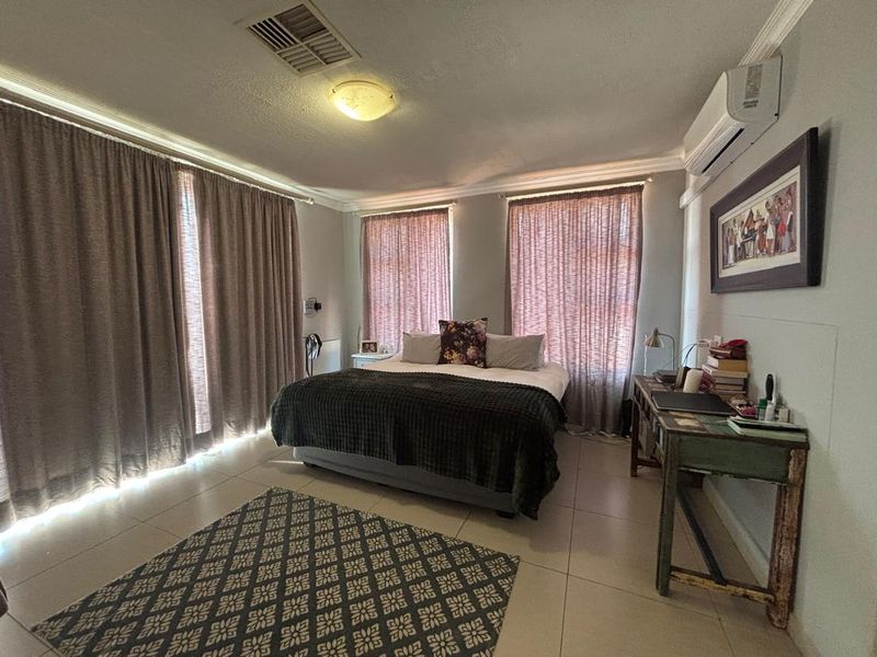 A well-lit bedroom featuring tiled flooring, crown molding, and a wall-mounted split-system air conditioner.