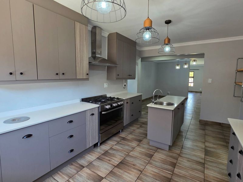 Modern kitchen featuring sleek cabinetry, stone countertops, a central island with sink, and stainless steel gas cooking appliances, finished with contemporary tiled flooring.