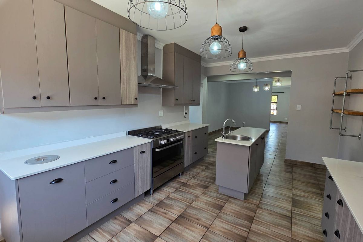 Modern kitchen featuring sleek cabinetry, stone countertops, a central island with sink, and stainless steel gas cooking appliances, finished with contemporary tiled flooring.