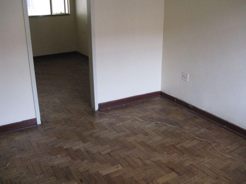 An empty living area featuring traditional herringbone parquet flooring and timber skirting boards, leading into an adjacent room.