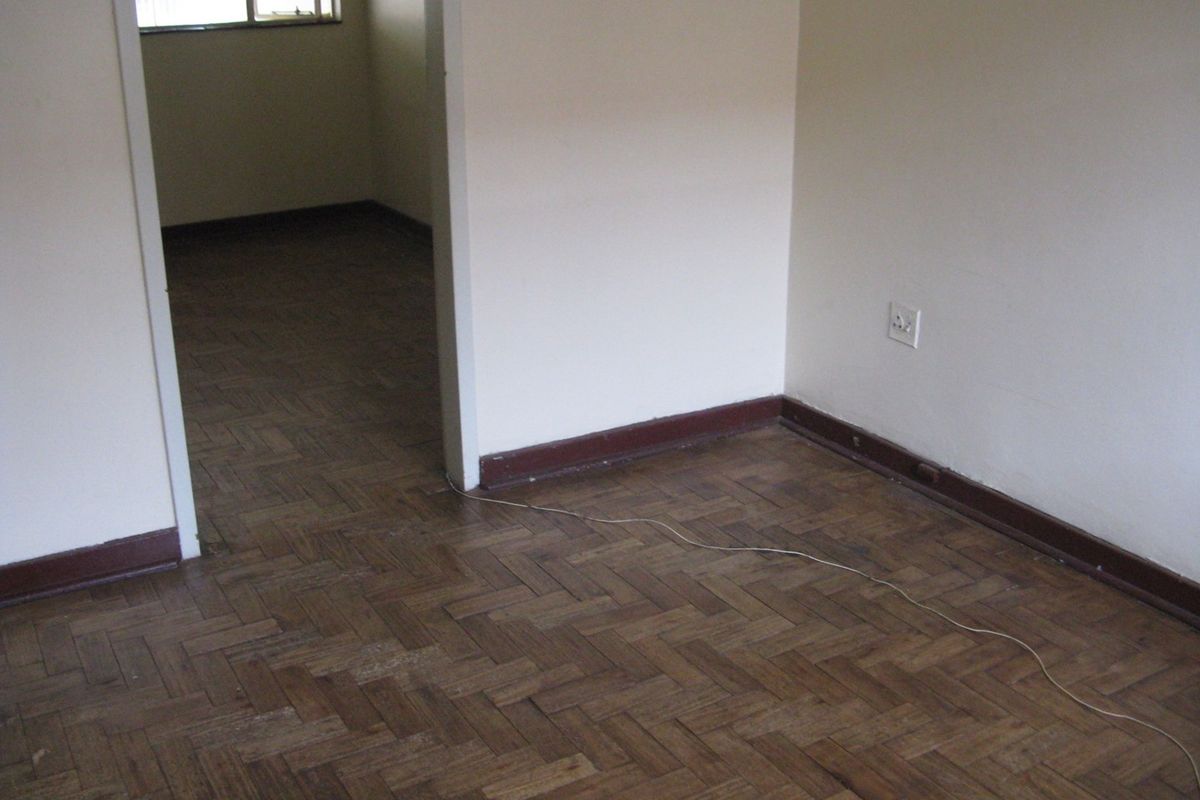 An empty living area featuring traditional herringbone parquet flooring and timber skirting boards, leading into an adjacent room.