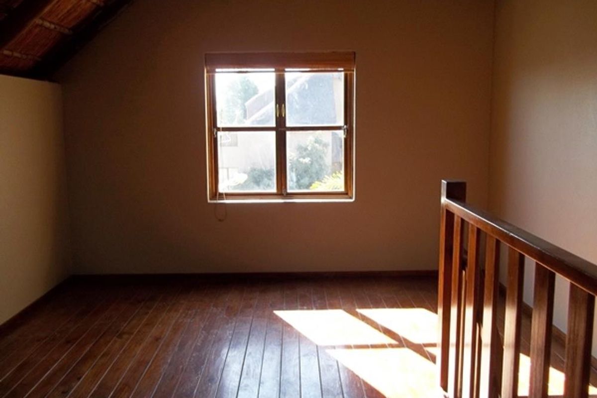 An attic-style bedroom featuring timber flooring, a sloped ceiling, and a wooden balustrade overlooking the lower level.