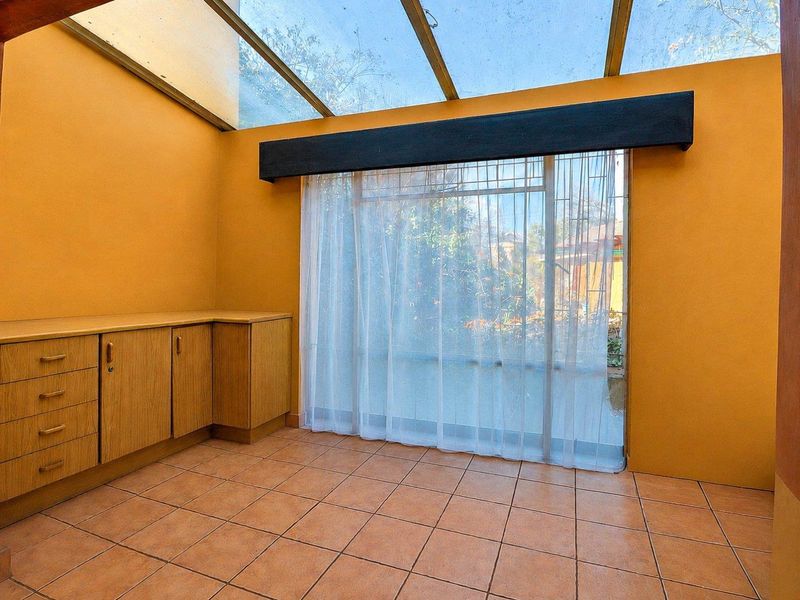 A sunroom or enclosed patio featuring a glass roof, tiled flooring, and built-in wooden cabinetry, offering a bright and versatile living space.