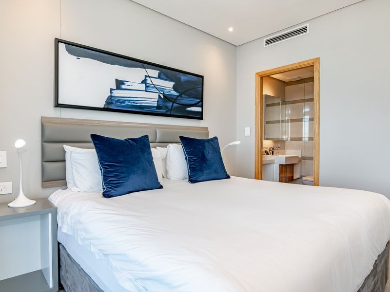 A modern, well-maintained bedroom featuring a neutral color palette, upholstered headboard, and direct access to an en-suite bathroom.