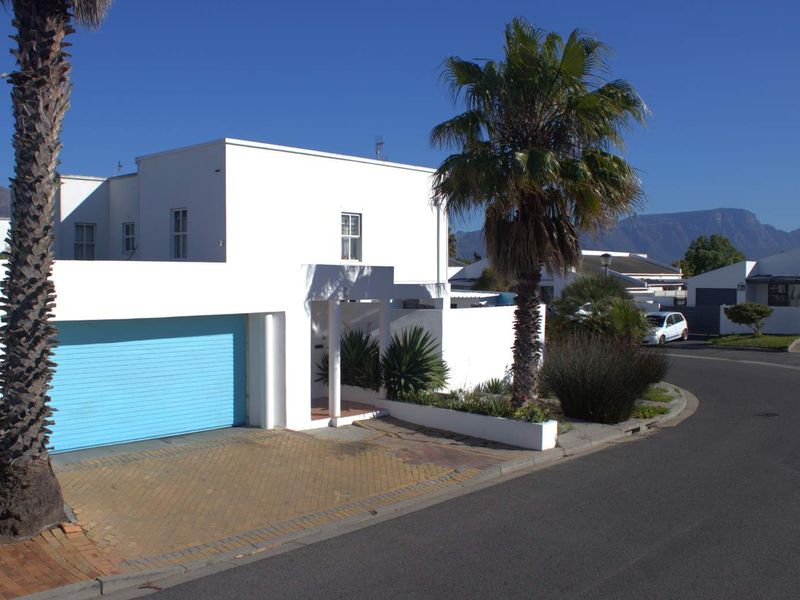 Front exterior view of a modern white house featuring a blue garage door, paved driveway, and established palm trees.