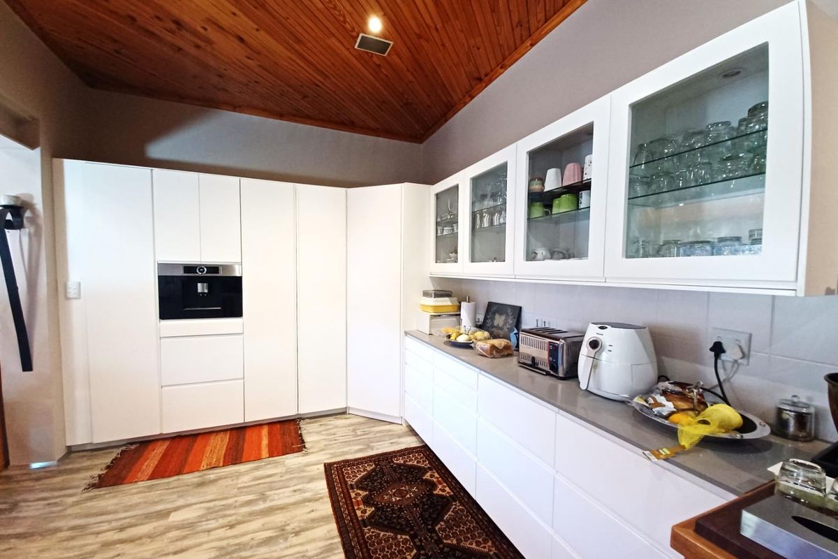 Modern kitchen featuring white cabinetry, integrated oven, glass-fronted upper cabinets, and a distinctive timber-paneled vaulted ceiling.