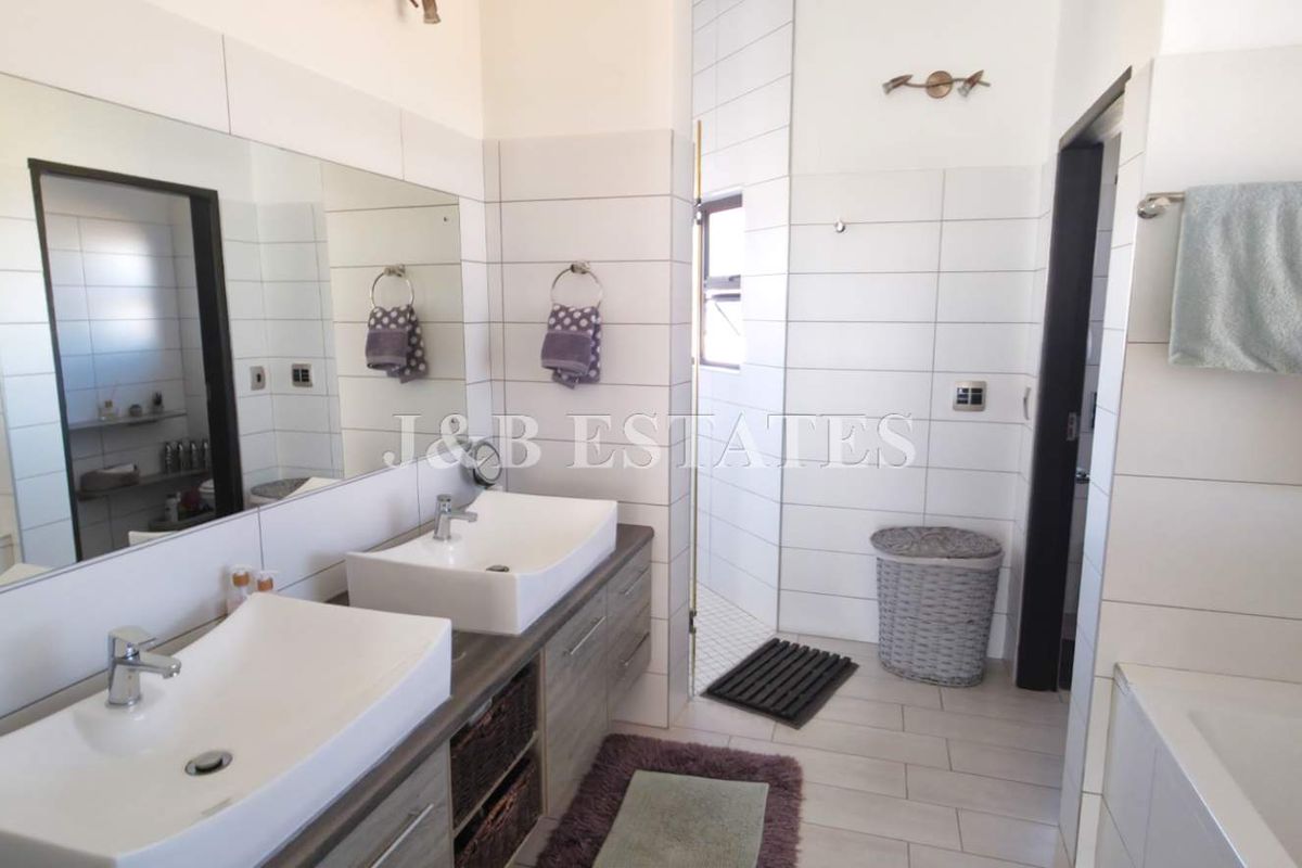 Modern bathroom featuring a double vanity with vessel sinks, large wall-mounted mirror, tiled walls, and a separate bathtub area.