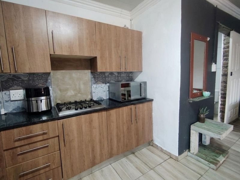 Compact kitchen featuring wood-look cabinetry, granite countertops, and a gas hob, complemented by tiled flooring and decorative backsplash detailing.