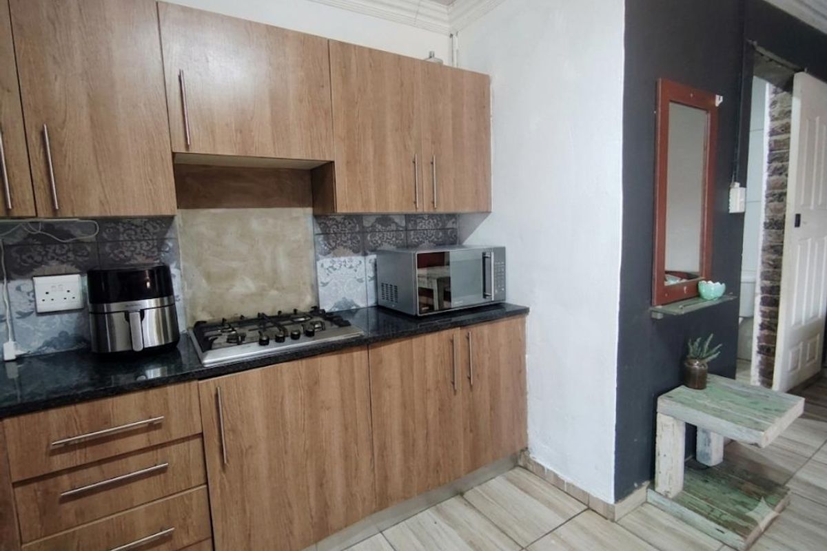 Compact kitchen featuring wood-look cabinetry, granite countertops, and a gas hob, complemented by tiled flooring and decorative backsplash detailing.
