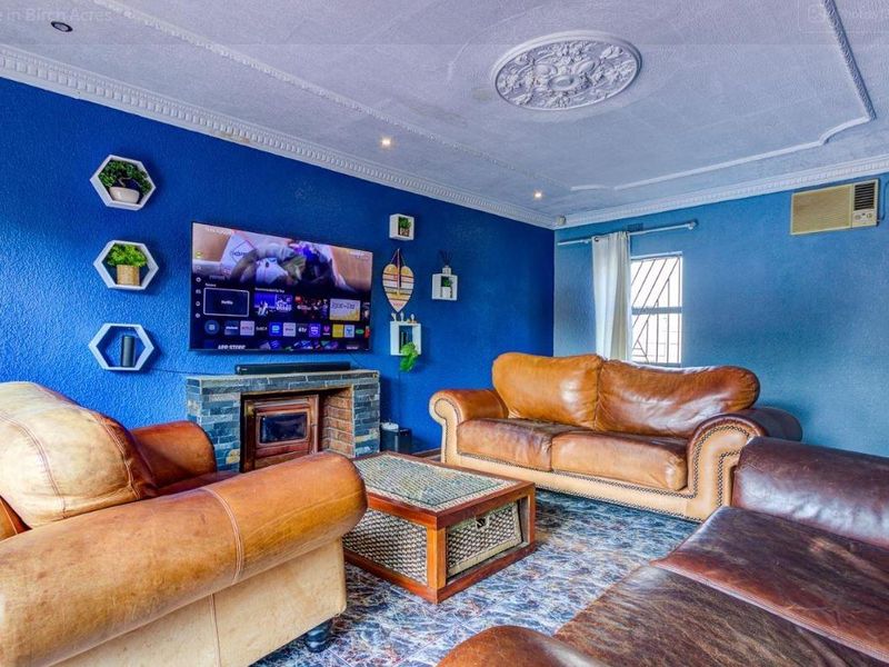 A living room featuring a stone-clad fireplace, decorative ceiling rose, and coving, finished with a bold blue wall and window-mounted air conditioning unit.