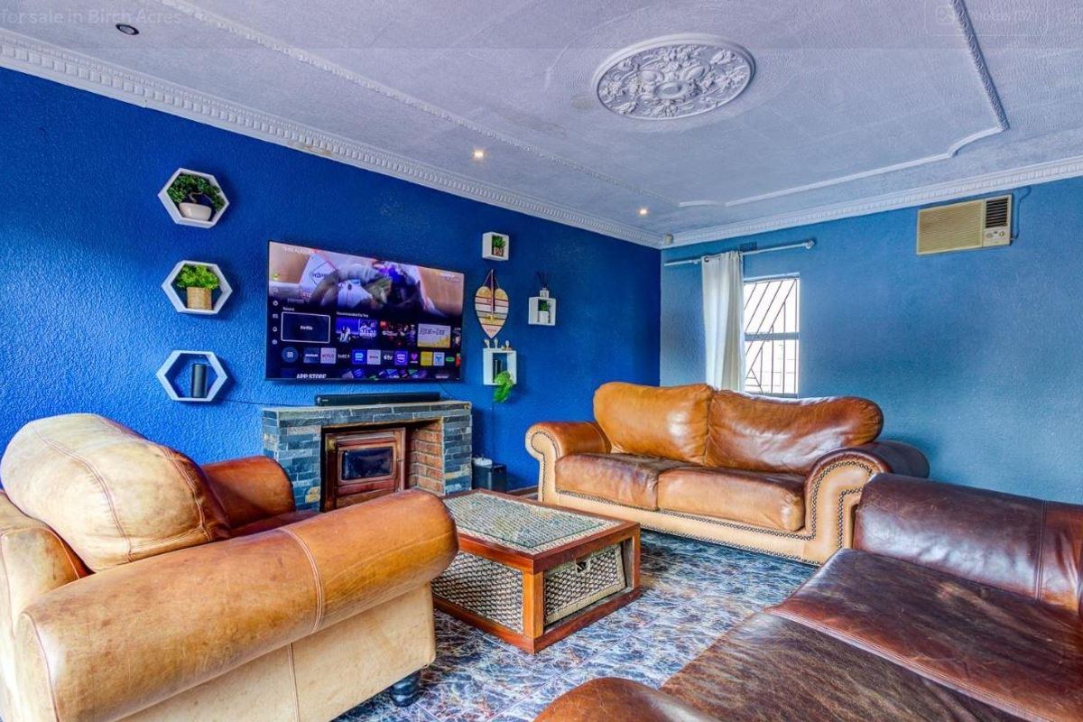A living room featuring a stone-clad fireplace, decorative ceiling rose, and coving, finished with a bold blue wall and window-mounted air conditioning unit.