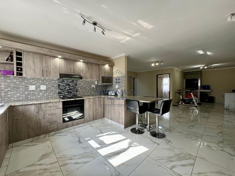Spacious open-plan kitchen and living area featuring modern wood-finish cabinetry, granite countertops, marble-look floor tiles, and a built-in fireplace.
