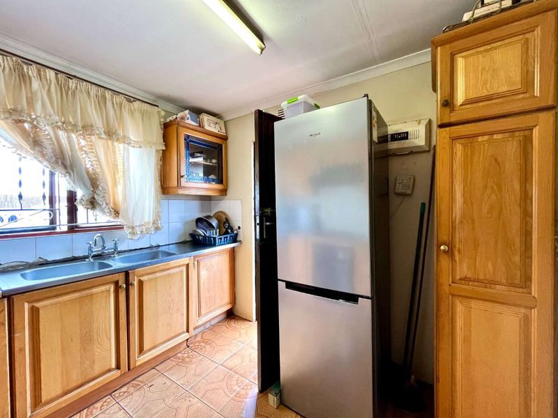 A functional kitchen featuring wooden cabinetry, a double basin sink, and tiled flooring, offering potential for a modern renovation.