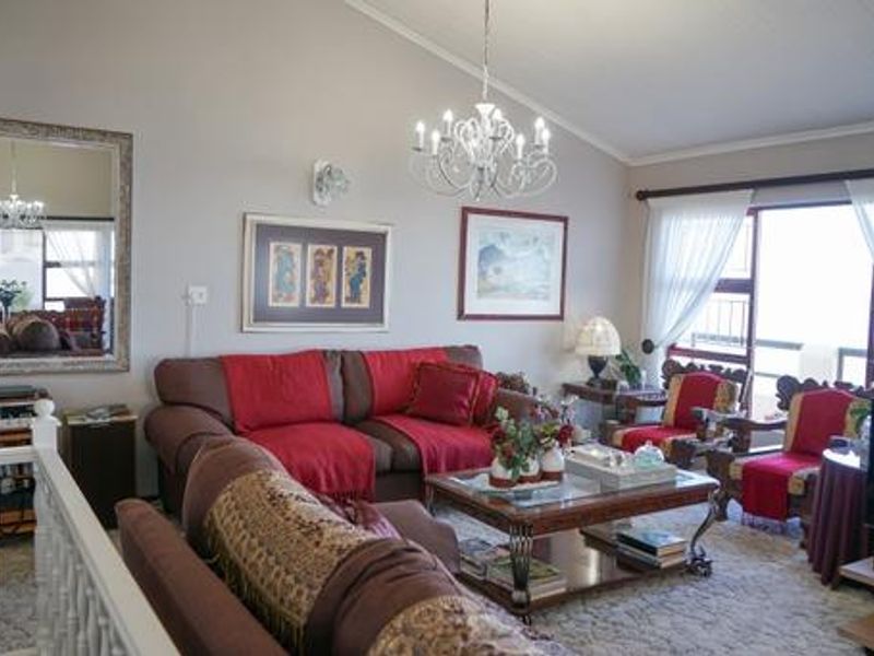 Spacious living room featuring a vaulted ceiling, elegant chandelier, and large sliding glass doors providing natural light and access to the exterior.