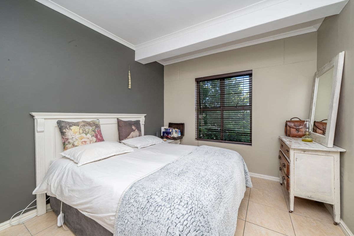 A well-maintained bedroom featuring neutral wall tones, tiled flooring, and a window fitted with venetian blinds.