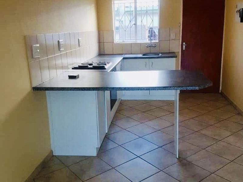 A functional kitchen featuring built-in cabinetry, a breakfast counter, integrated hob and oven, tiled backsplash, and ceramic floor tiles.