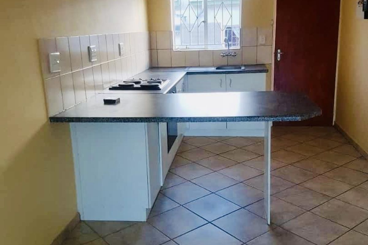 A functional kitchen featuring built-in cabinetry, a breakfast counter, integrated hob and oven, tiled backsplash, and ceramic floor tiles.