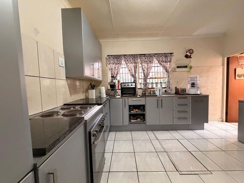 A functional kitchen featuring grey built-in cabinetry, granite countertops, an electric hob, and tiled flooring with a neutral splashback.