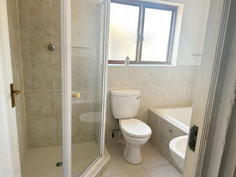 A functional bathroom featuring a shower enclosure, bathtub, toilet, and tiled finishes, offering a clean and practical layout.